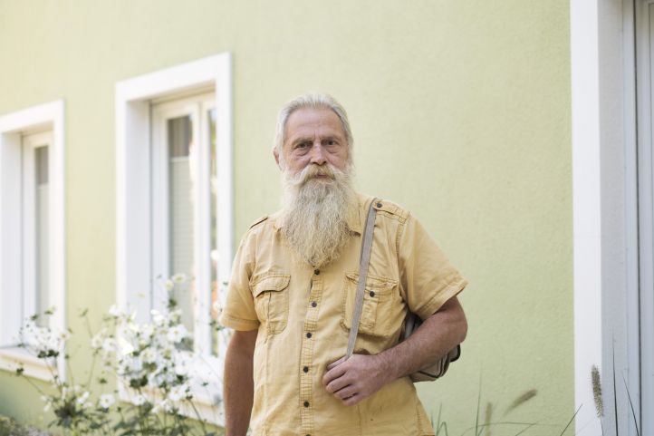 Ein älterer Mann, ein Senior, ein Rentner, ein alter Mann, mit langem weißem Bart und gelben Hemd schaut in die Kamera