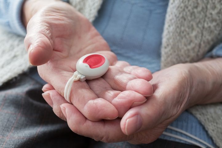 Zwei Hände einer alten Frau halten roten Hausnotrufknopf