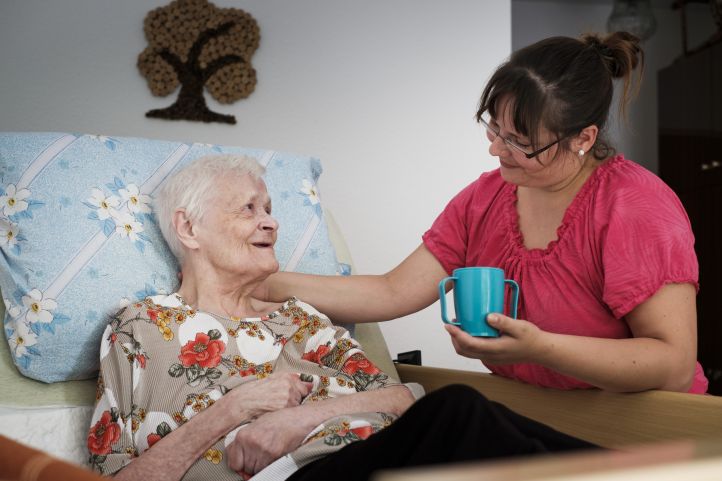 Pflegekraft hilft ältere Frau im Bett beim Trinken