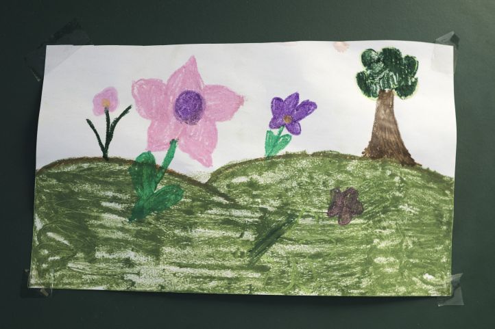 Eine Kinderzeichnung mit einer grünen Wiese, Blumen und einem Baum 