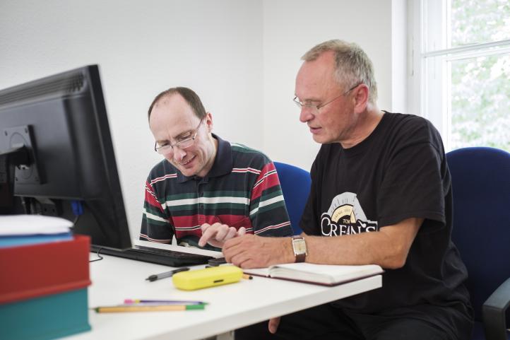 Zwei Männer sitzen an einem Computer und einer von ihnen tippt auf der Tastatur