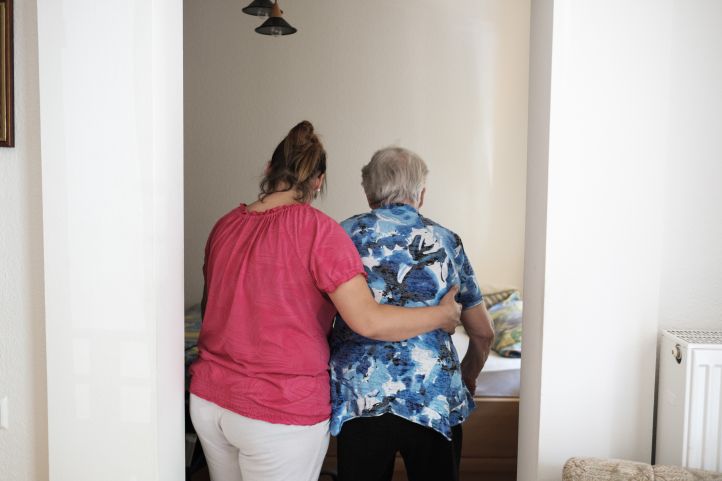 Eine Frau hilft einer alten Frau Seniorin am Bett in einem Pflegeheim