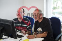 Zwei Männer sitzen an einem Schreibtisch und blicken gemeinsam in einen Monitor