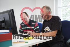 Zwei Männer sitzen am PC, während der eine dem anderen etwas erklärt