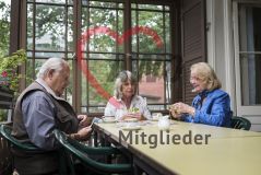 Zwei elegante Seniorinnen und ein älterer Herr sitzen an einem Tisch und spielen Karten