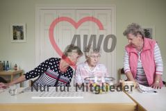 Zwei ältere Damen sehen einer dritten Frau dabei zu, wie sie am Tisch sitzend Kleingeld zählt