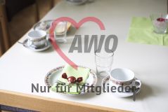 Ein Tischgedeck bestehend aus Kaffeetasse, Wasserglas und einem kleinen Kuchenteller dekoriert mit grüner Serviette und rotem Bonbon