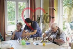 Eine Frau hilft einer alten Frau Seniorin beim Essen neben weiteren Seniorinnen und Senioren in einer Einrichtung