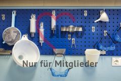 Arbeitsgeräte Sieb Trichter Schutzbrille Spritze hängen an einer Wand in einem Labor