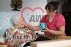 Eine Frau hilft einer alten Frau Seniorin im Bett beim Trinken und sie lächeln sich an