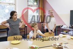 Zwei Mädchen und ein Junge stehen an einem Tisch mit Essen in einer Einrichtung