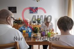 Mehrere alte Frauen und Männer Seniorinnen und Senioren sitzen an einem Tisch und eine Frau schält Kartoffeln
