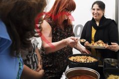 Vier Frauen kochen gemeinsam und legen sich lachend etwas Essen auf den Teller