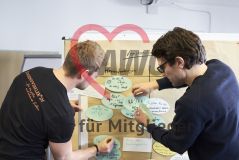 Zwei junge Männer heften Schilder Moderationskarten an eine Pinnwand Workshop Seminar