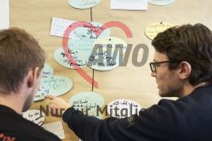 Zwei junge Männer stehen vor einer Pinnwand und sprechen miteinander über die Schilder Moderationskarten