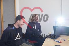 Zwei jungen Männer sitzen an einem Arbeitstisch mit Laptop Notebook Rechner Stiften Flyern und lachen