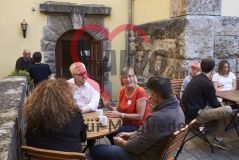 Mehrere Personen sitzen an einem Tisch mit Tassen auf einer Terrasse und unterhalten sich gut gelaunt in der Kaffeepause