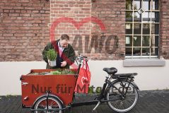 Mann an einem mit Pflanzen beladenem Lastenrad, am Lenker ein roter AWO-Beutel