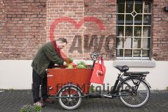 Mann an einem mit Pflanzen beladenem Lastenrad, am Lenker ein roter AWO-Beutel