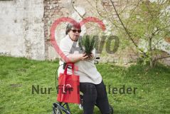 Frau im Rollator mit rotem AWO-Beutel hält eine Pflanze