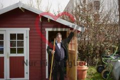 Mann mit Gartenhacke an der Tür eines roten Gartenschuppens
