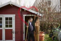 Mann mit Gartenhacke an der Tür eines roten Gartenschuppens
