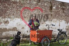 Frau nimmt vor einem Beet Pflanzen aus einem Lastenrad, daneben sitzt ein Hund