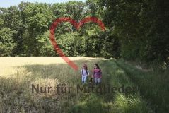 zwei Mädchen auf einem Feld, daneben Wald