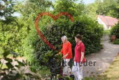Seniorin mit Rollator und Pflegerin im Garten