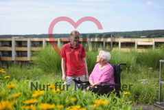 Seniorin im Rollstuhl und Pflegerin im Garten